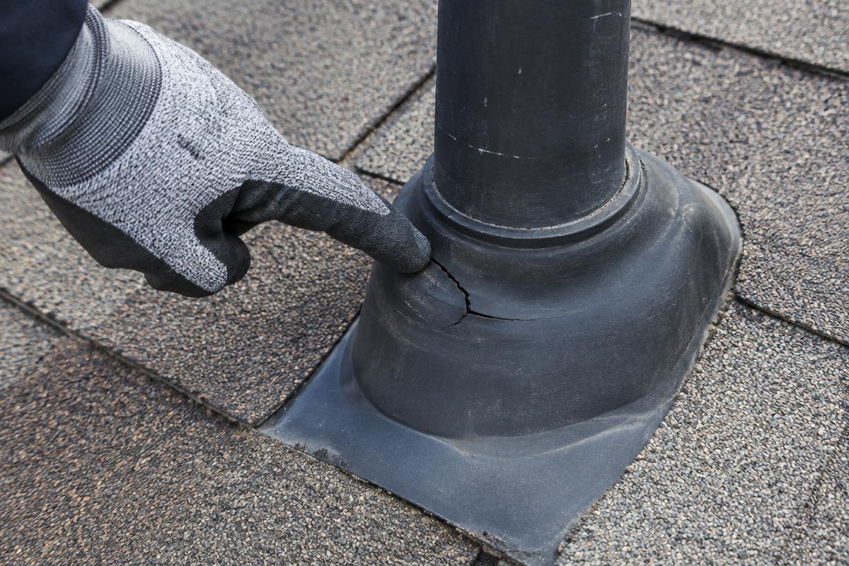 Roofer pointing to a cracked rubber pipe boot during an inspection